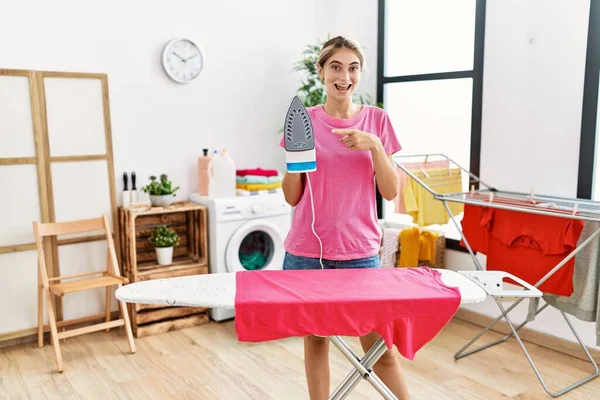 Joven Mujer Rubia Planchando Ropa Casa Sonriendo Feliz Señalando Con —  Fotos de Stock