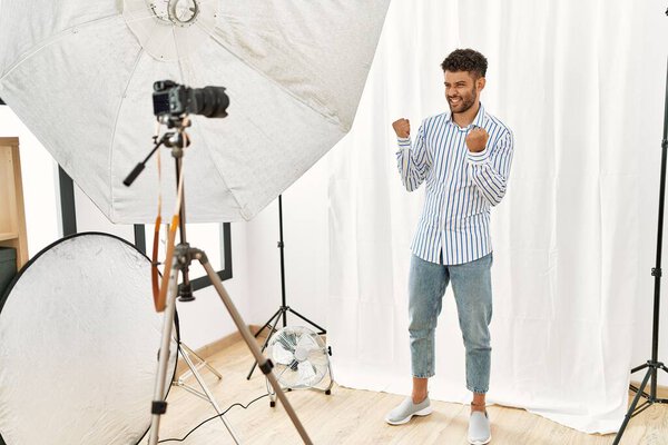 Arab young man posing as model at photography studio very happy and excited doing winner gesture with arms raised, smiling and screaming for success. celebration concept. 