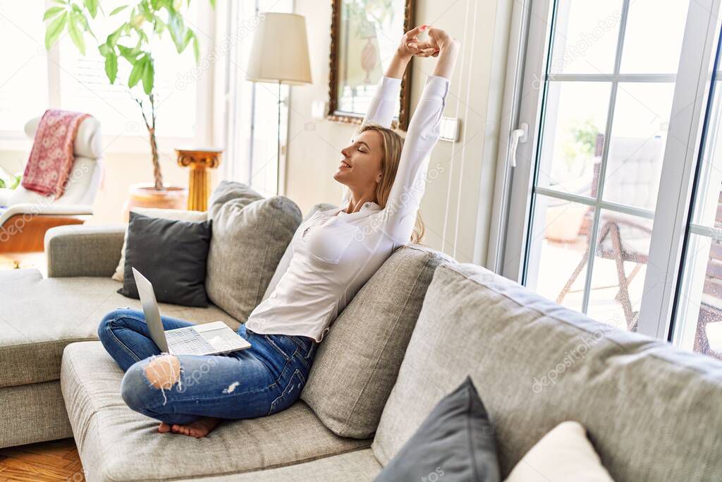 Young blonde woman stretching arms using laptop at home.