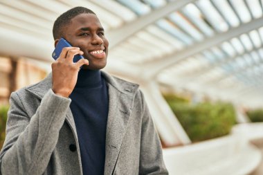 Genç Afrikalı Amerikalı gülümseyen mutlu bir adam şehirdeki akıllı telefondan konuşuyor.