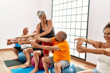 Bir grup orta yaşlı insan spor merkezinde kişisel antrenörleriyle birlikte formda top oynuyorlar..