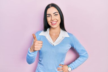 Pembe arka planda duran mavi gözlü güzel bir kadın elleriyle mutlu bir jest yapıyor. Kameraya bakıp başarıyı gösteren ifade. 