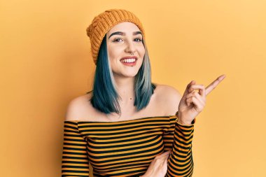 Yüzünde büyük bir gülümseme olan yünlü şapka takan genç modern bir kız, kameraya el ve parmak ile bakıyor.. 