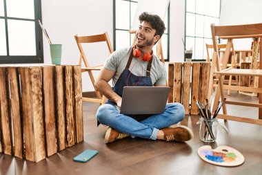 Sanat stüdyosunda kulaklık ve dizüstü bilgisayar kullanan İspanyol genç bir sanatçı..