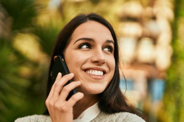 Genç İspanyol kadın gülümsüyor. Şehirdeki akıllı telefondan konuşuyor..