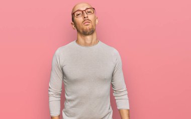 Sakallı, sıradan kıyafetler giyen ve gözlüklü kel bir adam. Yüzünde ciddi bir ifadeyle rahatlamış. Basit ve doğal bir şekilde kameraya bakıyorsun.. 