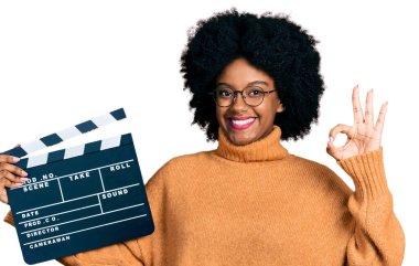 Genç Afro-Amerikalı kadın elinde video film klasörü tutuyor parmaklarıyla imza atıyor, gülümseyerek mükemmel bir sembol oluşturuyor. 