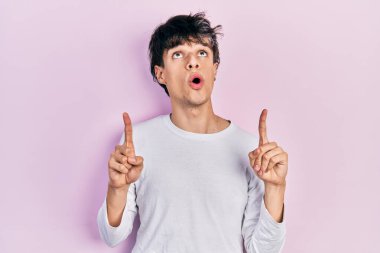 Yakışıklı hippi genç adam, gündelik beyaz tişört giyip şaşkın şaşkın yukarı bakıyor, parmaklarıyla işaret ediyor ve kollarını kaldırıyordu.. 