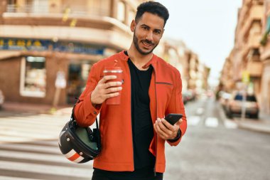 Genç İspanyol adam akıllı telefon kullanıyor. Şehirde kahve kaskı içiyor..