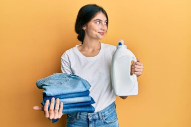 Çamaşır yıkayan, çamaşır deterjanı şişesi ve katlanmış kot pantolon giyen genç beyaz bir kadın.. 