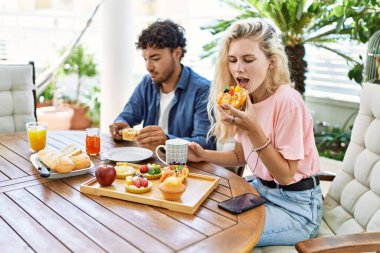 Genç çift, mutlu bir şekilde gülümsüyor. Kahvaltıyı terasta yapıyorlar..