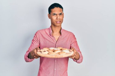 Genç Afro-Amerikan adam elinde kek tepsisiyle habersiz ve kafası karışık bir ifade tutuyor. şüphe kavramı. 