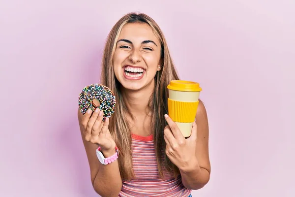 ドナッツを食べてコーヒーを飲んでいる美しいヒスパニック系の女性は笑顔で大声で笑います — ストック写真