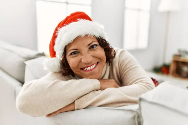Μεσήλικας Ισπανίδα Χαμογελαστή Ευτυχισμένη Φορώντας Χριστουγεννιάτικο Καπέλο Καθισμένη Στον Καναπέ — Φωτογραφία Αρχείου