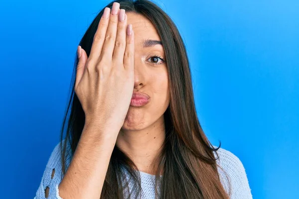 Young hispanic girl covering half face with hand puffing cheeks with funny face. mouth inflated with air, catching air.
