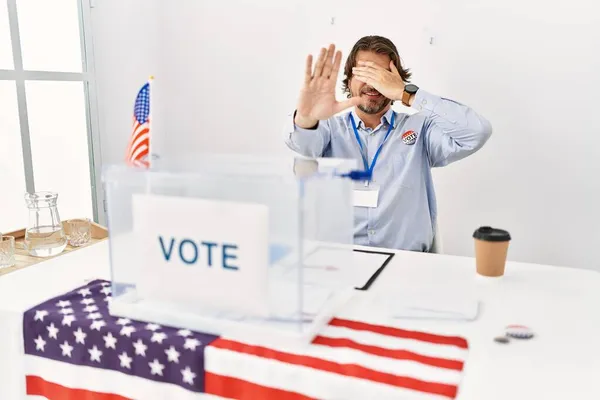 一个英俊的中年男人坐在投票站里 双手捂着眼睛 用忧郁和恐惧的表情做着停止的手势 尴尬和消极的概念 — 图库照片