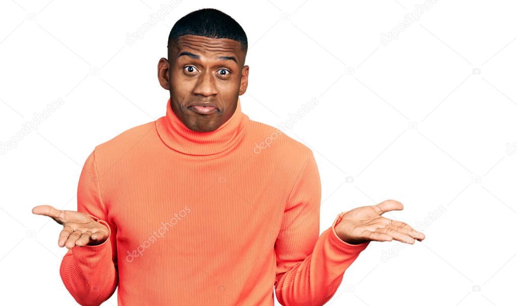 Young black man wearing orange turtleneck sweater clueless and confused expression with arms and hands raised. doubt concept. 