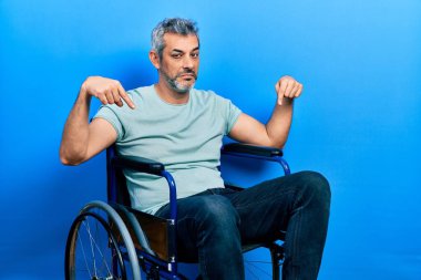 Yakışıklı, orta yaşlı, gri saçlı, tekerlekli sandalyede oturan üzgün ve üzgün görünen, yönünü parmaklarıyla gösteren mutsuz ve depresif bir adam.. 