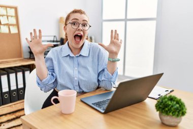 Ofiste çalışan genç kızıl saçlı kadın bilgisayarla on numarayı gösterip işaret ederken kendinden emin ve mutlu bir şekilde gülümsüyor.. 