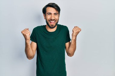 Gündelik beyaz tişört giyen genç İspanyol adam kollarını kaldırıp, gözleri açık bir şekilde başarıyı kutluyor ve şaşırıyor. Kazanan konsept. 