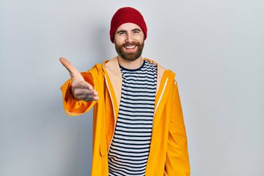 Sakallı, sarı yağmurluk giyen, dostça el sıkışarak selamlaşan beyaz bir adam. başarılı iş. 