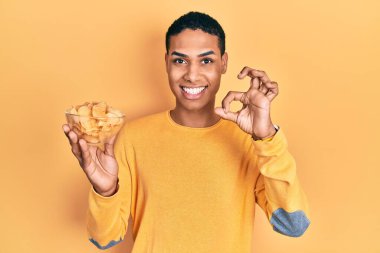 Genç Afrikalı Amerikalı adam patates cipsi tutuyor. Parmaklarıyla imza atıyor, gülümsüyor. Mükemmel bir sembol. 