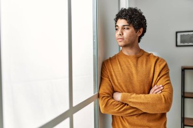 Ciddi yüz ifadesi olan genç bir İspanyol evde kollarını kavuşturup duruyor..