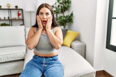 Genç esmer kadın evdeki kanepede oturuyor. Korkmuş ve şok olmuş. Şaşırmış ve şaşırmış bir halde. 