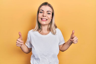 Güzel beyaz tişört giyen beyaz kadın. Başarı işareti yapıyor. Elleriyle olumlu jest yapıyor. Neşeli ifade ve kazanan jest. 