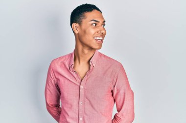 Genç Afro-Amerikalı, günlük kıyafetler giymiş, yüzünde gülümseme ve doğal bir ifadeyle yan yana bakıyor. Kendinden emin gülen. 