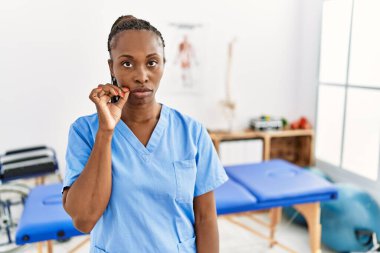 Saçları örgülü zenci bir kadın. Klinikte çalışıyor. Ağzı ve dudakları parmaklarıyla kapalı. gizli ve sessiz, tabu konuşması 