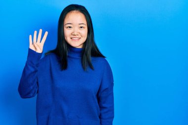 Genç Çinli kız gündelik giysiler giyer ve parmaklarını dört numara ile gösterir ve gösterirken kendinden emin ve mutlu gülümserdi.. 