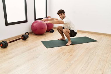 Genç İspanyol adam gülümsüyor spor merkezinde kendine güvenen bacak egzersizi yapıyor.