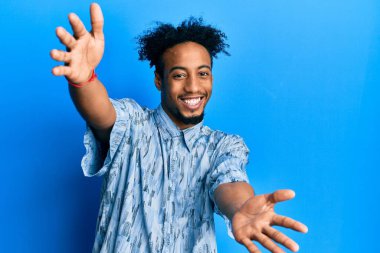 Sakallı, sıradan giyinmiş, kucaklaşmak için kollarını açıp kameraya gülümseyen Afro-Amerikan bir genç. Mutluluğu kucaklayan neşeli bir ifade.. 