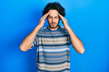 Pembe arka planda günlük kıyafetler giyen yakışıklı İspanyol bir adam. Başı ağrıdığı için başının üstünde. Stres yüzünden. migren ağrısı. 