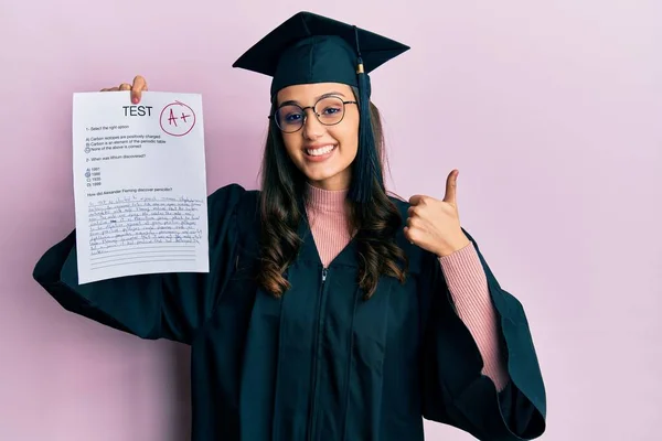 身穿毕业服的年轻惊慌失措的女人 满面春风 高高兴兴地举行了考试 竖起大拇指 签了字 — 图库照片