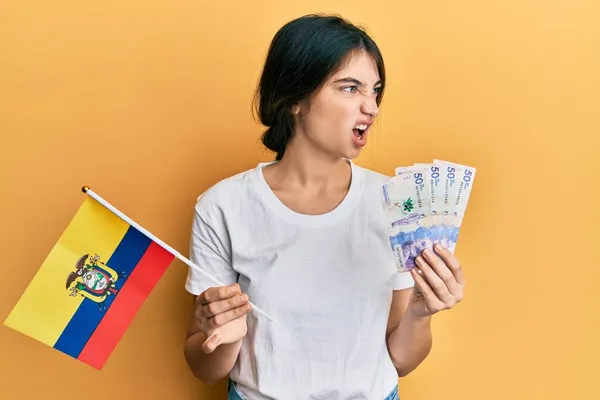 年轻的高加索女人拿着科洛姆比亚国旗和科洛姆比亚比索钞票 怒气冲冲地尖叫 怒气冲冲地大叫 愤怒和好斗的概念 — 图库照片