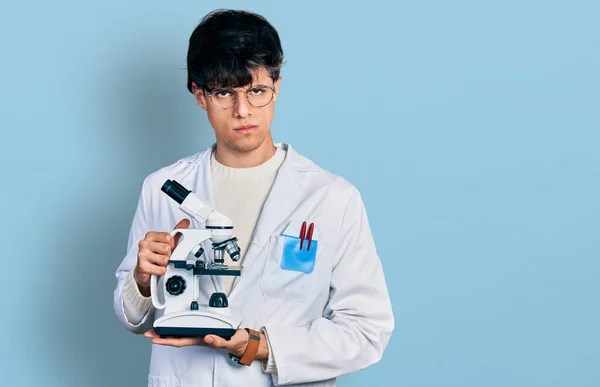 Όμορφος Χίπστερ Νεαρός Που Φοράει Εργαστηριακή Ποδιά Κρατώντας Μικροσκόπιο Σκεπτικός — Φωτογραφία Αρχείου