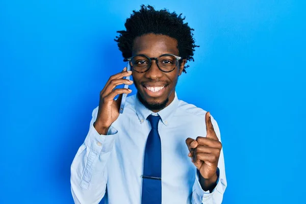 Young african american man having conversation talking on the smartphone smiling with an idea or question pointing finger with happy face, number one