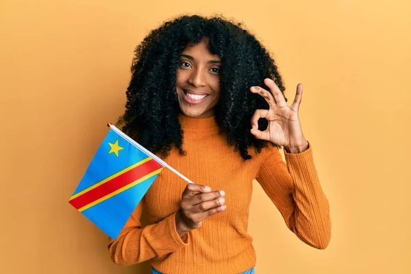 African american woman with afro hair holding democratic republic of the congo flag doing ok sign with fingers, smiling friendly gesturing excellent symbol