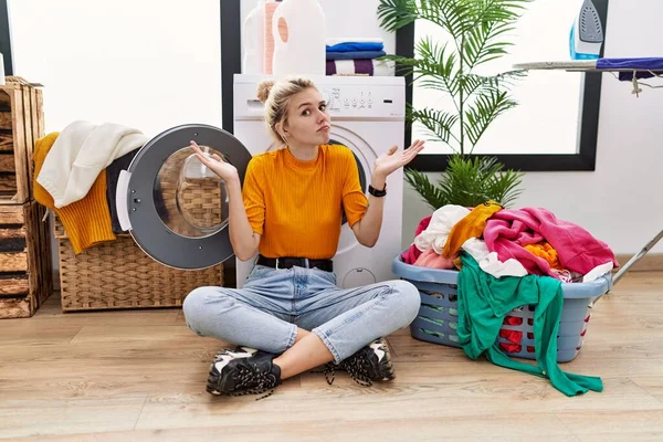 Jonge Blonde Vrouw Doet Zittend Bij Wasmachine Onwetend Verwarde Uitdrukking — Stockfoto