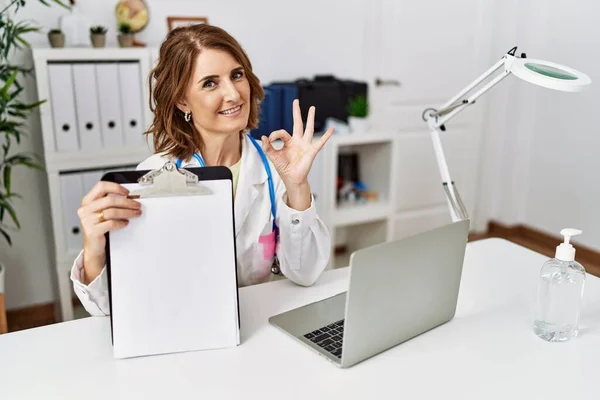 Middle Age Doctor Woman Holding Clipboard Blank Space Doing Sign — Stock Photo, Image