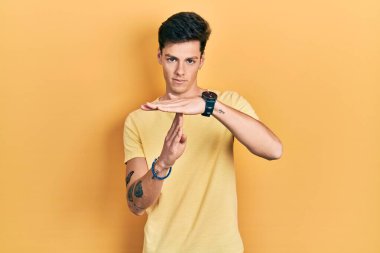 Gündelik sarı tişört giyen genç İspanyol adam. Elleriyle jest yapıyor, hayal kırıklığına uğramış ve ciddi bir yüz ifadesi takınıyor. 