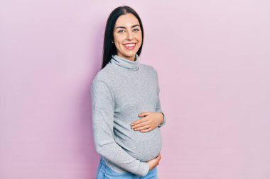 Mavi gözlü güzel bir kadın bebek bekliyor, hamile karnına dokunuyor mutlu ve serin bir gülümsemeyle. şanslı kişi. 