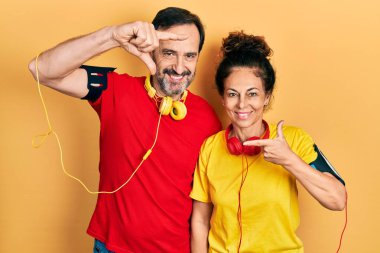 Orta yaşlı bir çift İspanyol kadın ve erkek spor giysisi ve kol bandı takıyor gülümsüyor elleri ve parmakları gülen yüzlü bir çerçeve yapıyorlar. yaratıcılık ve fotoğrafçılık kavramı. 