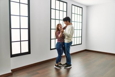 Genç İspanyol çift gülümsüyor boş yeni evde mutlu bir şekilde dans ediyor.