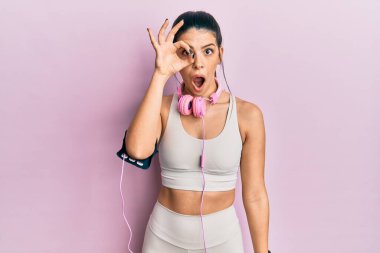 Spor kıyafetleri giyen ve kulaklık takan genç İspanyol kadın şaşırmış yüz ifadesiyle şaşırmış bir şekilde hareket ediyor ve parmaklarının arasından bakıyor. İnançsız ifade. 