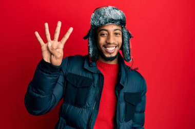 Sakallı, kışlık şapkalı ve paltolu genç Afrikalı Amerikalı dört numaralı parmaklarıyla işaret ederken kendinden emin ve mutlu gülümsüyor.. 