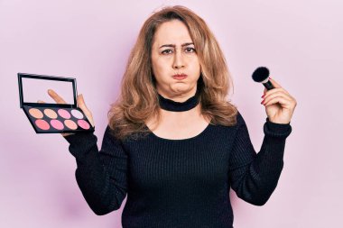 Makyaj fırçası tutan beyaz bir kadın ve komik yüzüyle yanakları kızarıyor. Ağzı havayla şişer, havayı yakalar.. 