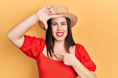 Yaz şapkası takan, gülümseyen, elleri ve parmakları gülen yüzlü genç İspanyol kadın. yaratıcılık ve fotoğrafçılık kavramı. 